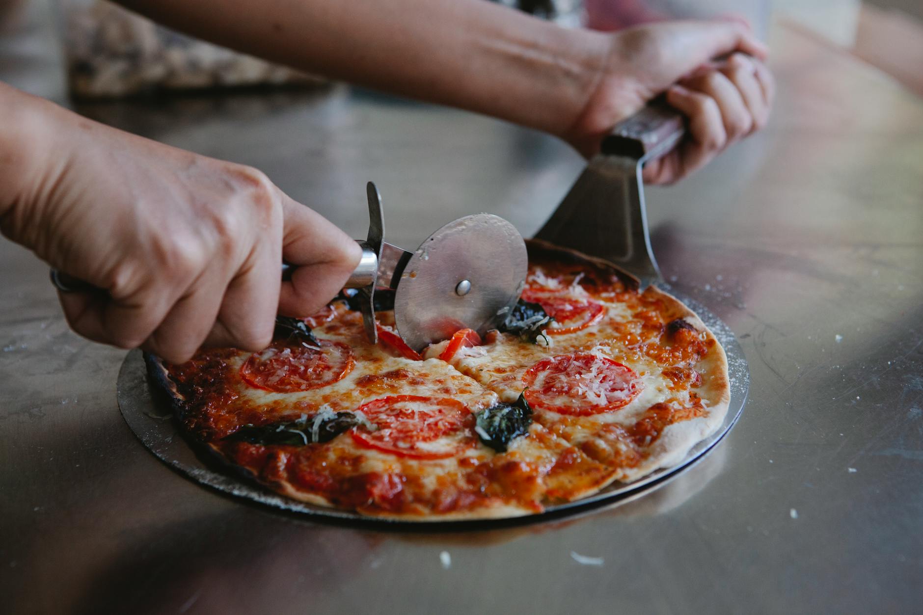 Ktoś kroi świeżo upieczoną pizzę z mozzarellą i bazylią