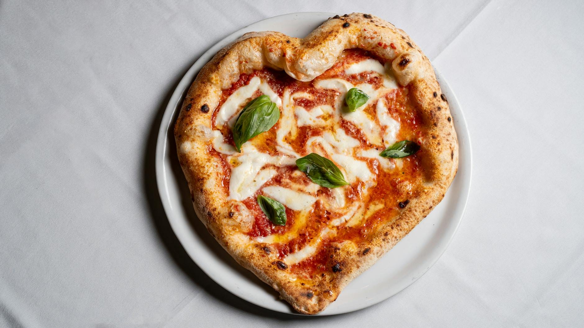 Serce z pizzy na cienkim cieście z mozzarellą i bazylią na białym talerzu