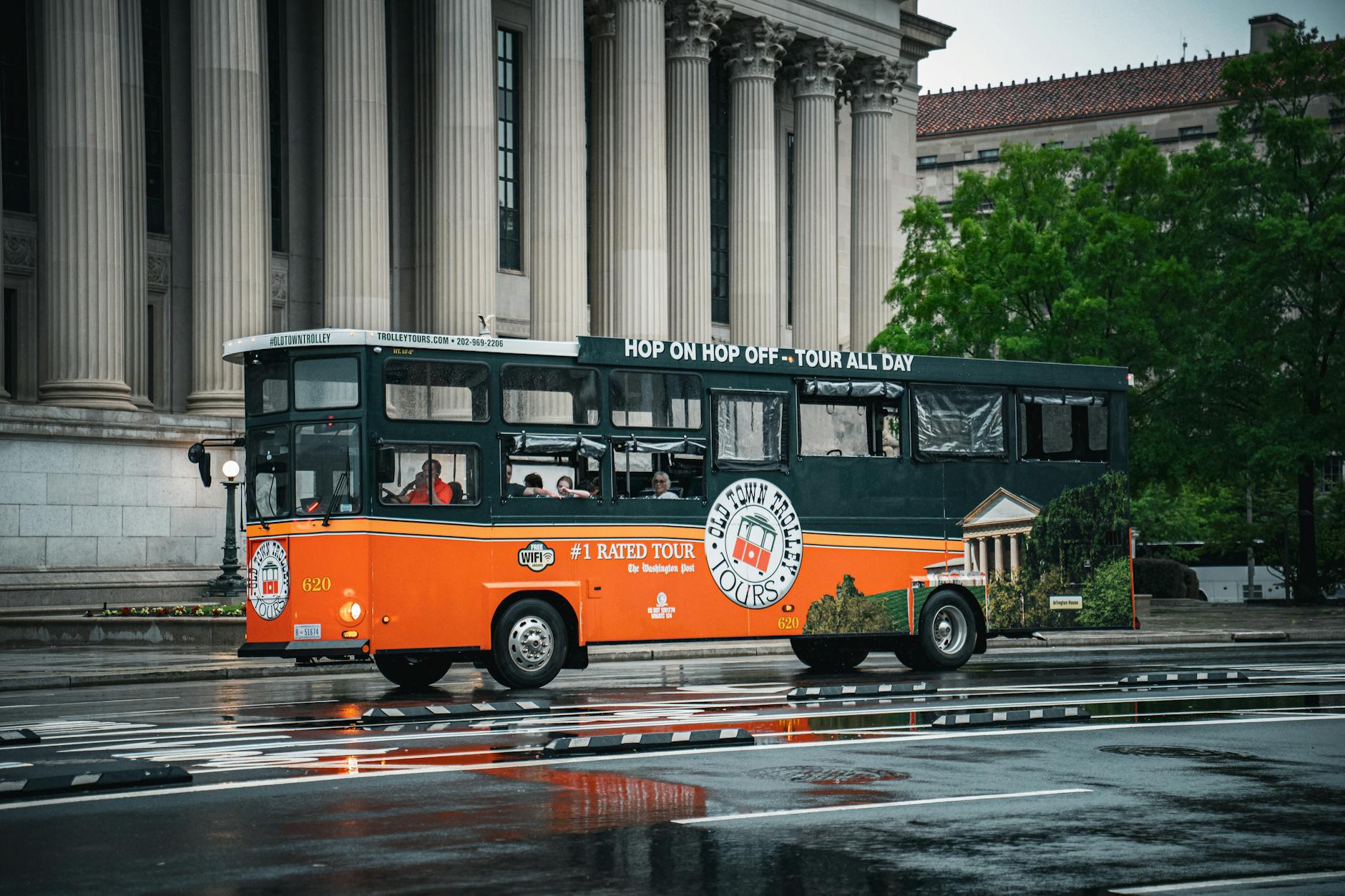 Czerwony autobus turystyczny na mokrej ulicy przed zabytkowym budynkiem