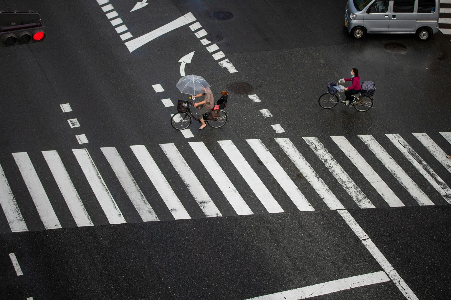 Rowerzyści z parasolami przejeżdżają przez deszczowe skrzyżowanie