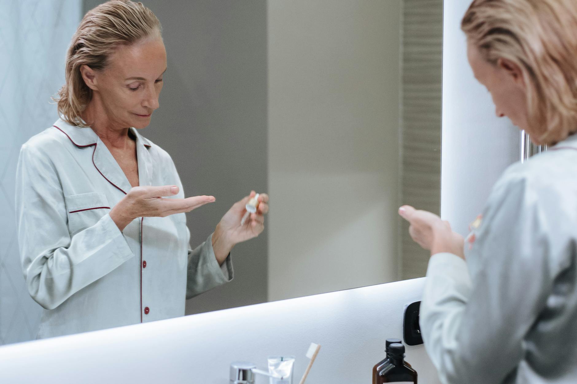 Starsza kobieta nakłada serum do twarzy przed lustrem w łazience