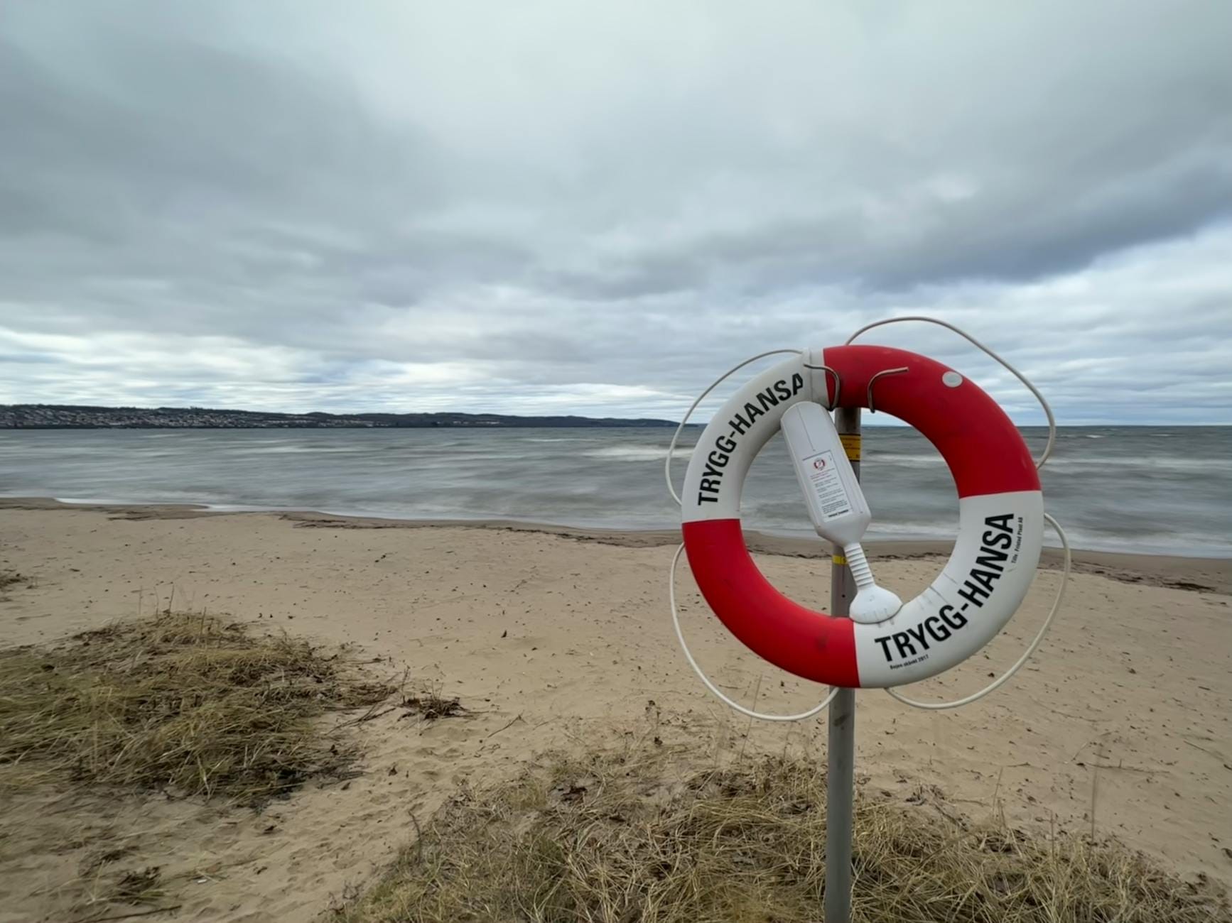 Czerwona koło ratunkowe Trygg-Hansa na pustej, pochmurnej plaży