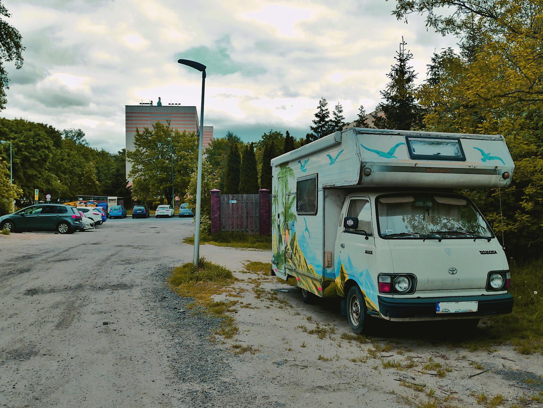 Kolorowy kamper zaparkowany przy ulicy wśród miejskich drzew i budynków