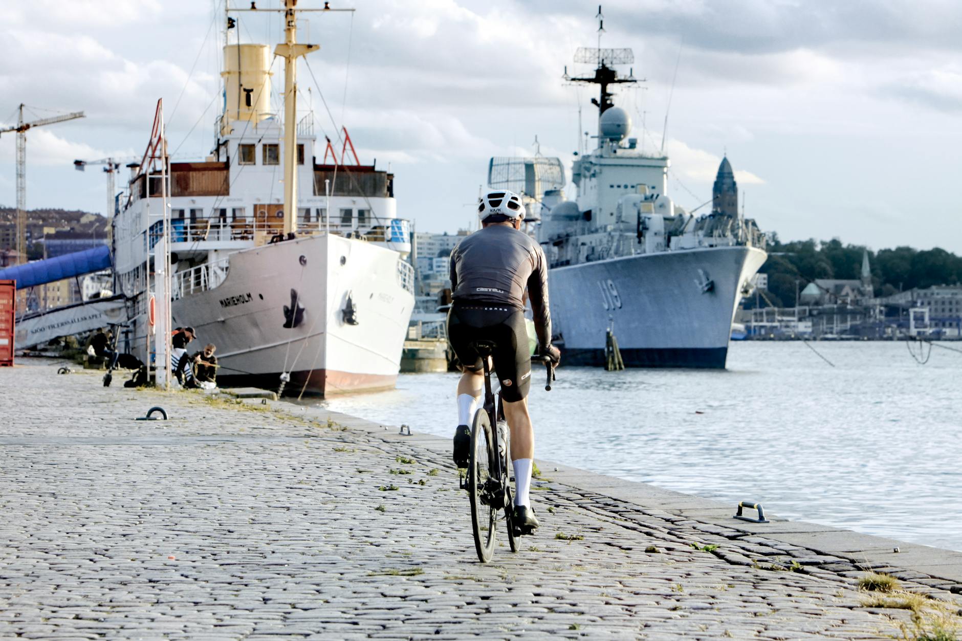 Kristiansand pieszo i rowerem: ścieżki, wypożyczalnie i zasady ruchu Rowerzysta jedzie wzdłuż nabrzeża z widokiem na statki i zabudowę miasta