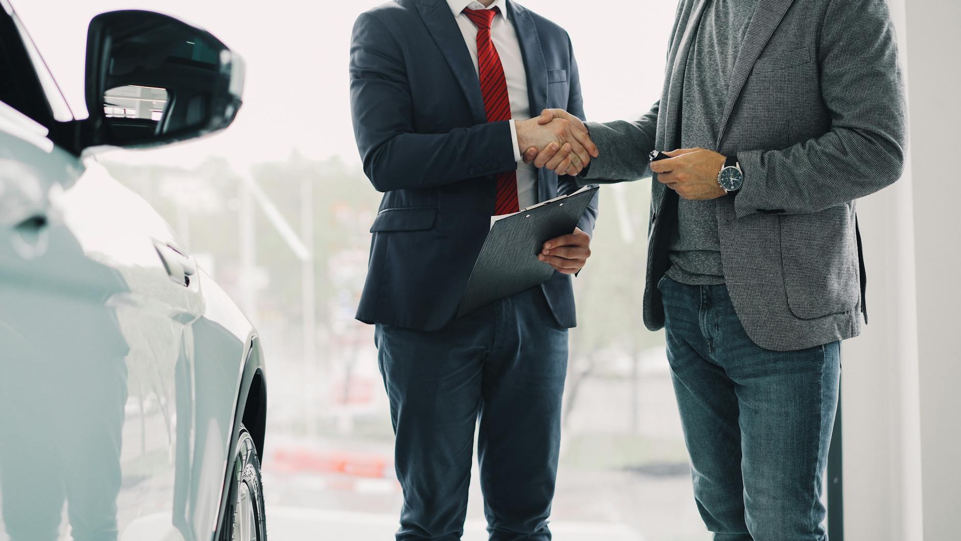 Dwaj mężczyźni podają sobie ręce przy wynajmie auta w salonie