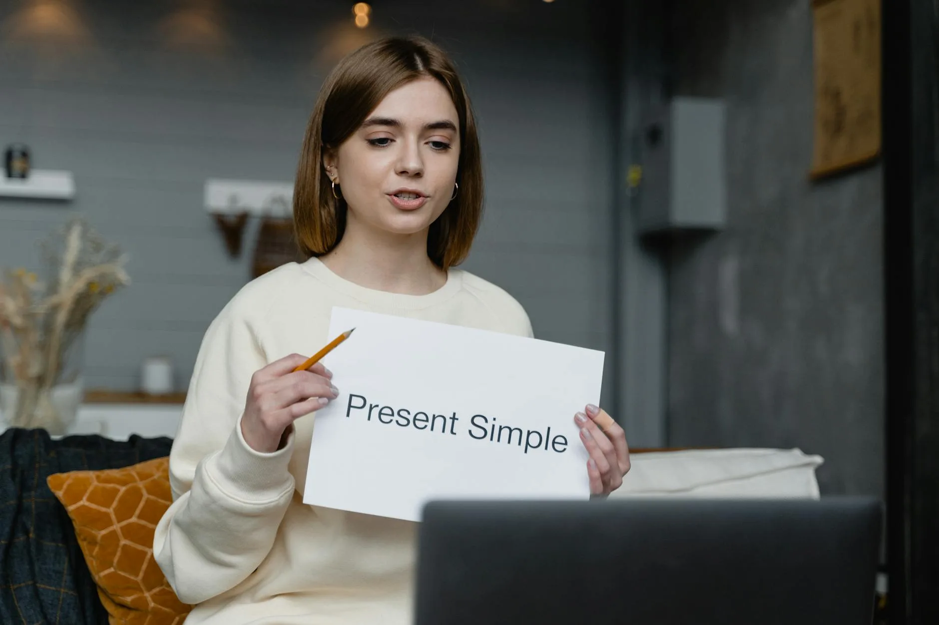 Jak zacząć naukę języka od zera i naprawdę zrobić postępy Młoda kobieta uczy angielskiej gramatyki online, trzyma notatkę Present Simple