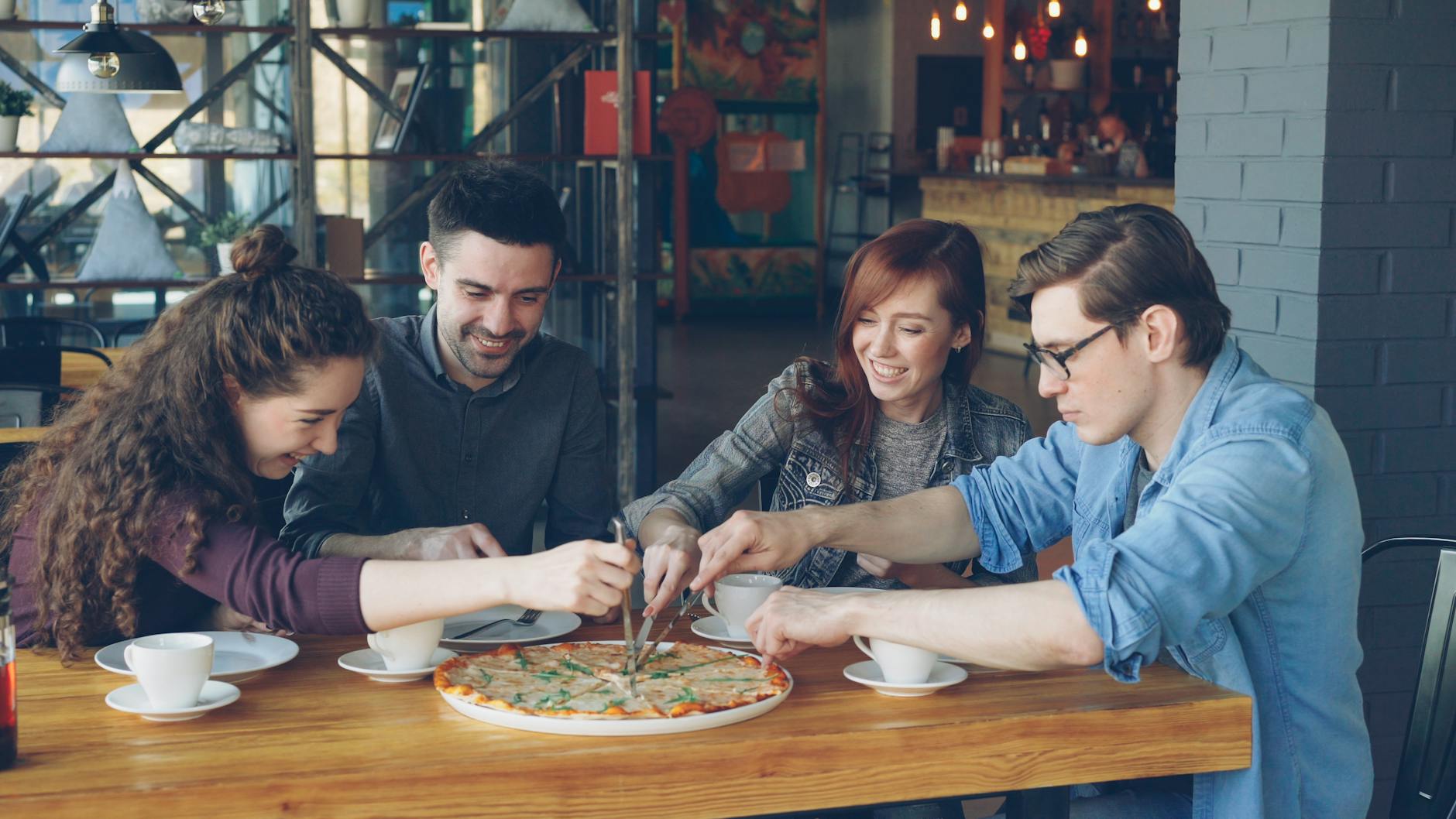 Młodzi dorośli dzielą się pizzą w niedrogiej, przytulnej kawiarni