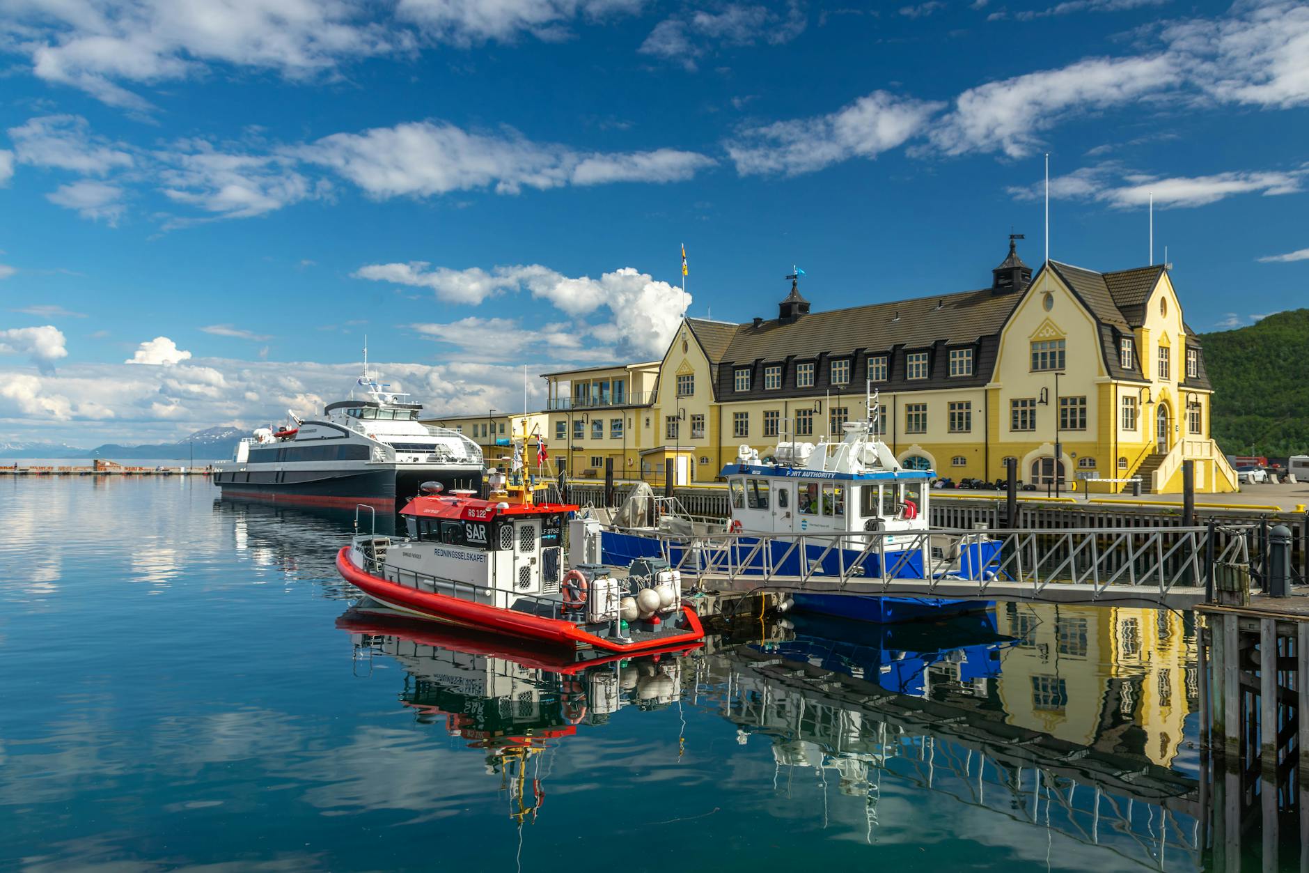 Słoneczny port w Harstad z zacumowanymi promami przy żółtym budynku