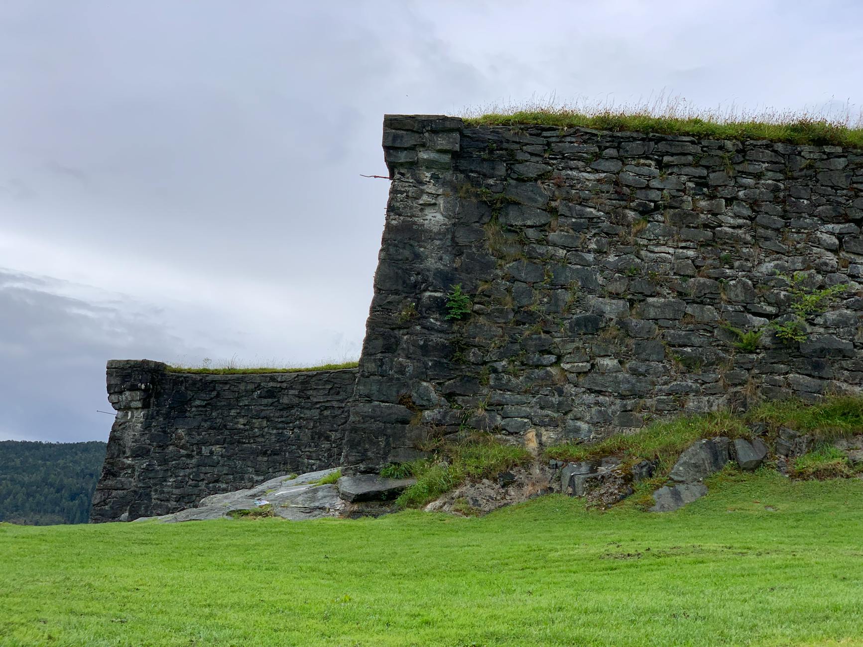 Kamienny mur fortu w Kristiansand otoczony zielenią pod pochmurnym niebem