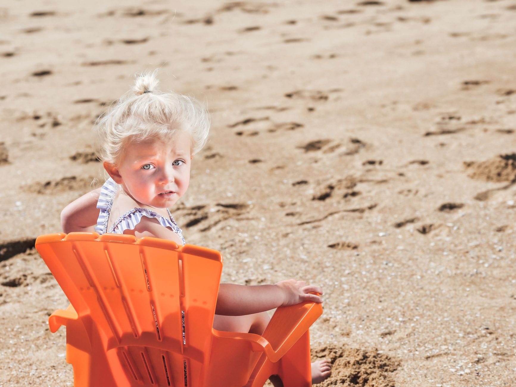 Małe blond dziecko na pomarańczowym krześle na piaszczystej plaży