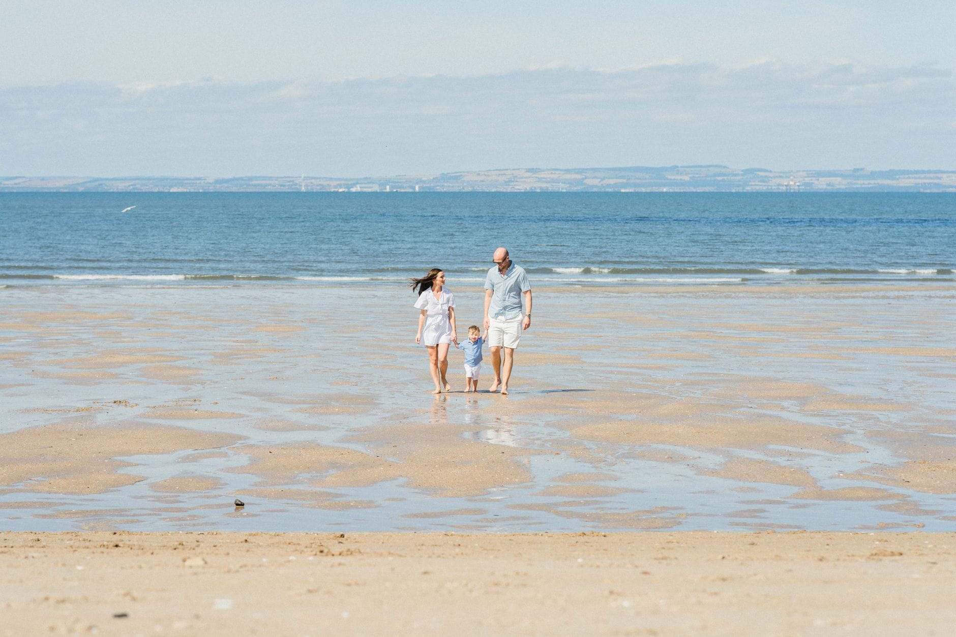 Rodzina z małymi dziećmi spaceruje po piaszczystej plaży w słoneczny dzień