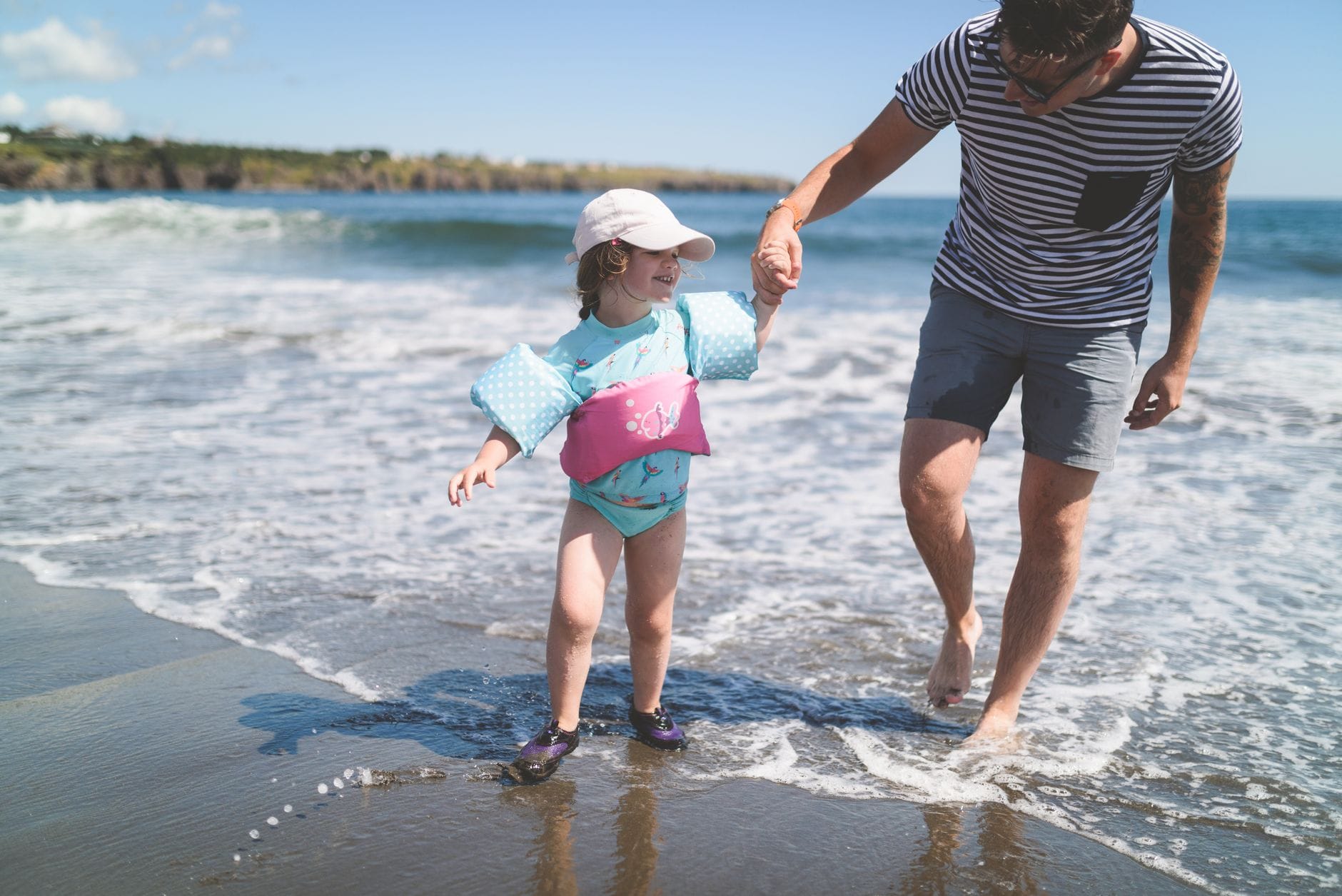 Tata trzyma dziecko za rękę na płytkiej, słonecznej plaży