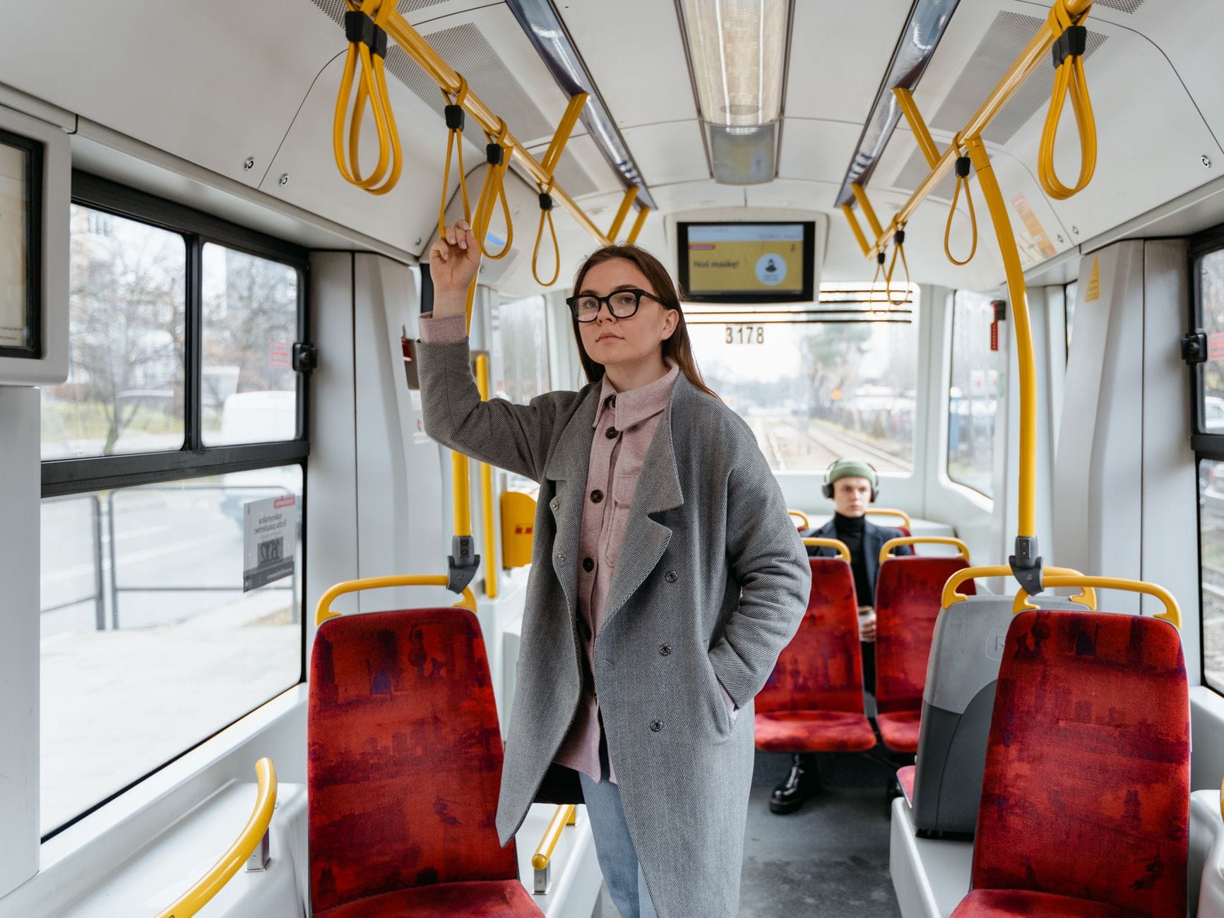 Kobieta w płaszczu stoi w tramwaju i trzyma się poręczy