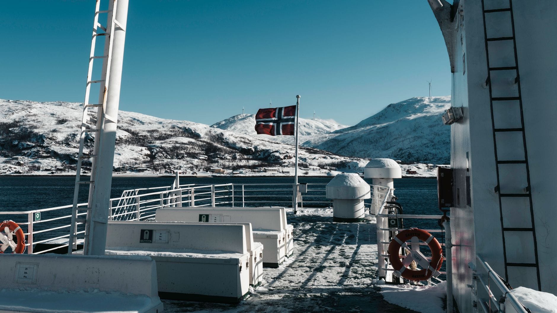 Pokład promu z flagą Norwegii i ośnieżonymi górami w tle