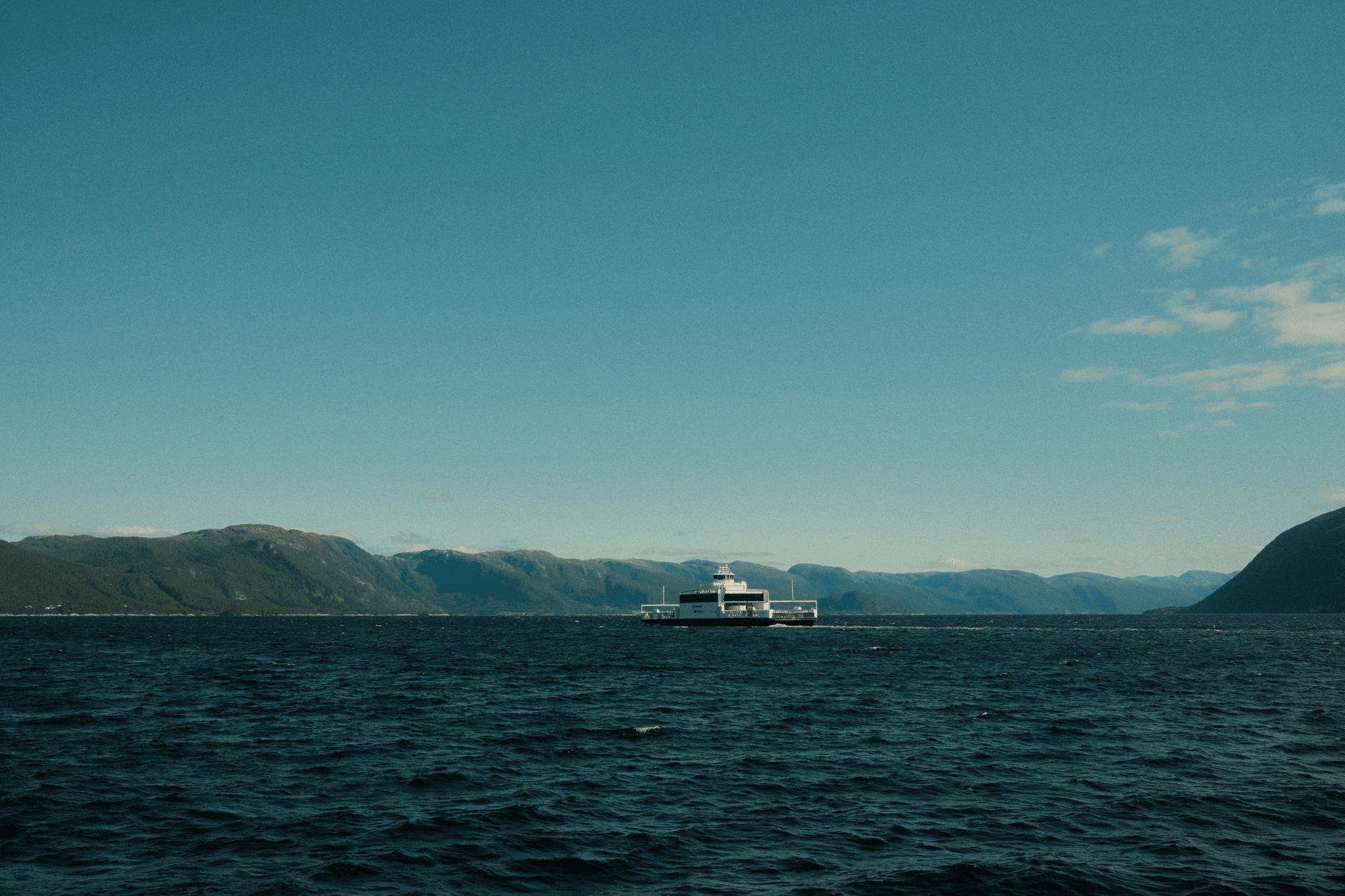 Prom płynie przez spokojny norweski fiord w słoneczny dzień