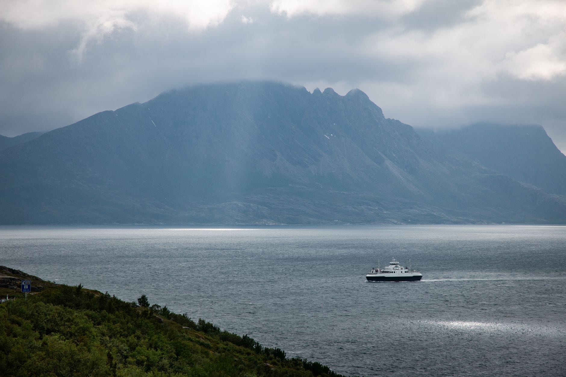 Prom płynie przez spokojny norweski fiord wśród mglistych gór